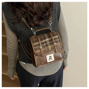 Détail d'un sac à dos vintage à carreaux marron avec écusson d'ours, porté par un mannequin