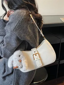 White minimalist baguette bag with gold buckle and plush bunny charm on gray knit sweater