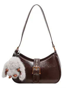 Deep brown crescent baguette bag in oil wax leather with a plush bunny charm on white background