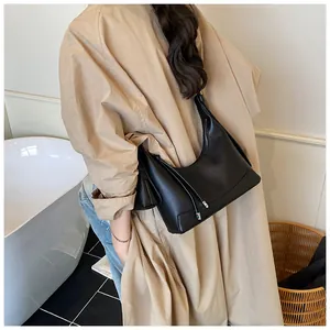 Vue latérale d'un sac baguette noir texturé porté avec un trench-coat beige chic