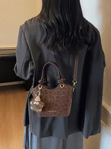 Sac seau léopard marron avec poignée nouée et breloque peluche porté par mannequin