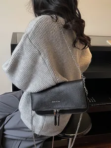 Sac baguette noir texture lychee avec bandoulière chaîne argentée porté par un mannequin