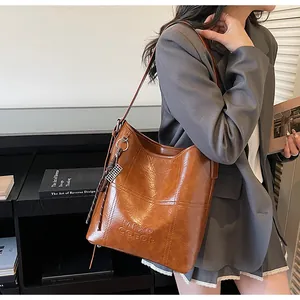 Close-up of brown oil-wax leather tote bag with embossed text and metallic charm detail