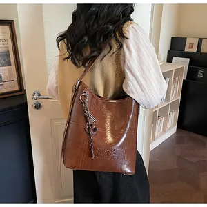 Close-up of a large brown leather tote bag featuring an embossed logo and woven pendant