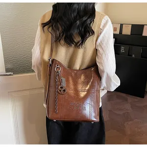 Detail of vintage brown oil wax leather tote featuring embossed logo and braided charm