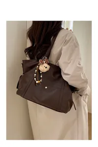 Detail of dark brown tote bag with metal buckle pocket and plush bear charm pendant