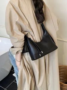 Sac hobo minimaliste en cuir noir grainé porté à l'épaule sur un trench-coat beige