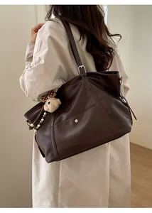 Detail of dark brown tote bag with plush bear charm on beige trench coat