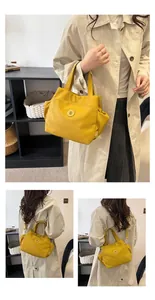 Détail du sac seau en nylon jaune montrant le logo en métal et la bandoulière amovible