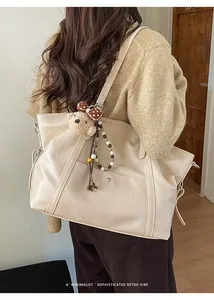 Close-up of a large cream tote bag with a plush bear charm and beaded strap on a model