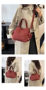 Détail du sac seau en nylon rouge brique avec logo métallique et bandoulières logotypées