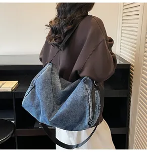 Detail of blue washed denim hobo bag with wide black strap and functional side zipper