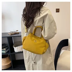Détail du sac seau en nylon jaune moutarde avec large bandoulière sur un manteau beige