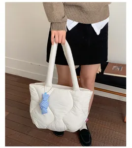 Detail of white quilted puffer tote bag with a blue plaid bow charm and wave stitching