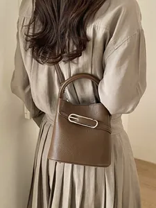 Minimalist dark brown lychee pattern bucket bag with silver buckle held by a model