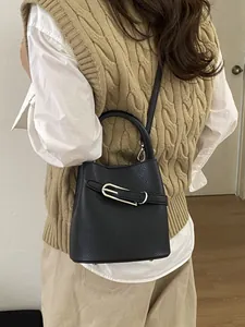 Minimalist black lychee leather bucket bag with gold hardware and shoulder strap