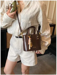 Détail du sac seau en cuir marron foncé avec pompon en perles et logo doré chic