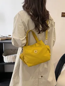 Sac seau tendance en nylon jaune vif avec large bandoulière porté avec un trench beige