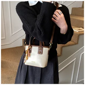 Détail du sac seau crème avec bordure marron et pendentif en perles de bois sur mannequin