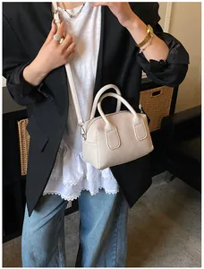 Mini sac Boston crème en cuir grainé porté avec une veste de blazer noire chic