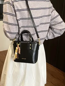 Sac seau chic en cuir noir avec breloque perlée présenté dans une scène de style de vie