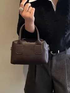 Sac Boston minimaliste en cuir grainé marron foncé porté par un mannequin de mode