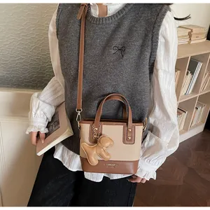 Close-up of brown bucket bag with plush puppy pendant and fine stitching details