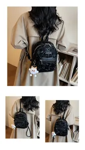Detail eines schwarzen Mini-Rucksacks mit Relieftextur und weißem Plüschtier-Anhänger