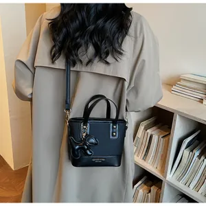 Detail view of a black retro crossbody bag with a cute dog charm on a trench coat model