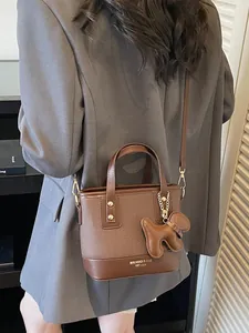 Modern brown contrast bucket bag with crossbody strap and cute puppy charm on model