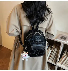 Detail eines schwarzen Mini-Rucksacks mit Buchstabenprägung und weißem Plüschtier