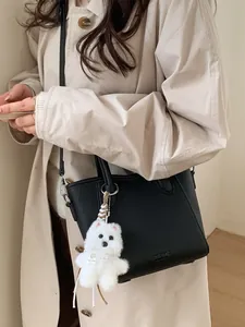 Sac seau en cuir grainé noir avec charme chiot et bandoulière sur trench-coat beige