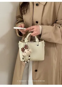 Detail of cream bucket bag with lychee grain texture and cute teddy bear pendant