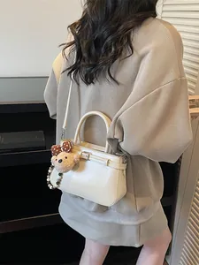 Cream bucket bag with teddy bear charm shown as a crossbody on a casual outfit