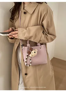 Detail view of pink leather bucket bag featuring a bear charm and beaded chain accessory