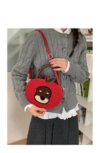 Detail of red apple-shaped plush crossbody bag with cute bear embroidery and leather handle