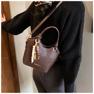 Detalle del bolso de mano marrón con colgante de cuentas y correa ajustable