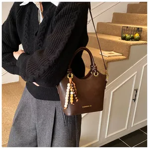 Detalle de bolso bucket de cuero mate marrón oscuro con borla de cuentas de madera