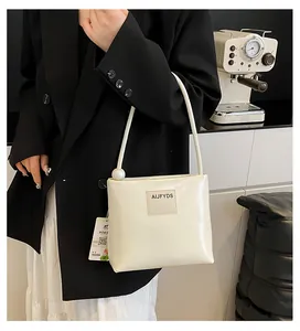 Dettaglio di una borsa a secchiello in pelle bianco crema con perla e targhetta