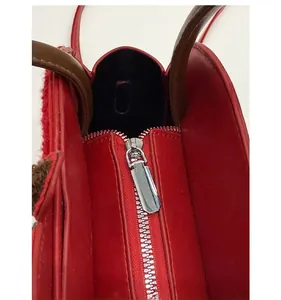 Close-up of smooth silver metal zipper and plush trim on red leather handbag