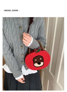 Detail of red apple-shaped plush handbag with dog embroidery held by a model