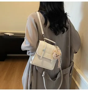 Detail shot of a cream crossbody bag with plaid pattern flap and plush bear charm