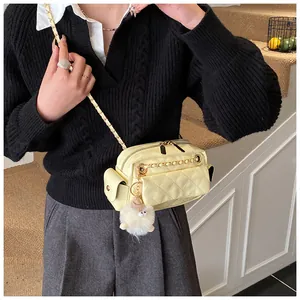 Detalle de un bolso bandolera acolchado crema con cadena dorada y pompón blanco de peluche