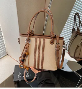 Detail of canvas bucket bag with brown leather trim and decorative wooden tassel