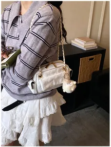 Detalle de bolso baguette blanco acolchado con cadena dorada y colgante de pompón suave