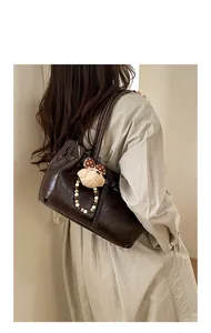 Detail of dark brown tote bag featuring glossy texture and plush doll charm with bow