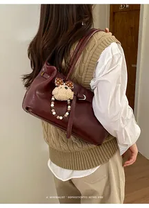 Detail view of burgundy leather tote bag with plush bear charm and beaded strap on shoulder