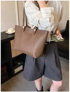 Detail of a brown tote bag featuring golden metal buckles and fine stitching on the handle