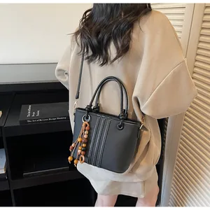 Detail of black bucket bag with wooden bead tassel and elegant vertical stitching texture
