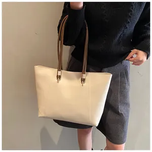 Detail view of large beige tote bag with brown straps and elegant gold metal hardware